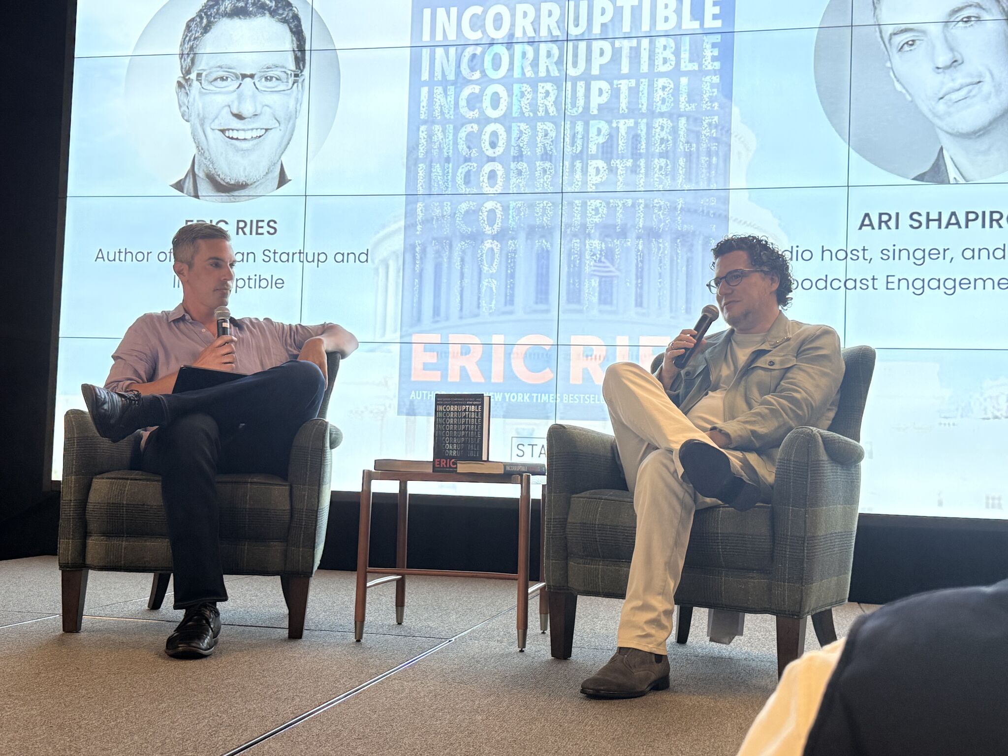 Eric Ries and Ari Shapiro in conversation on stage at STATION DC, with the Incorruptible cover projected behind them