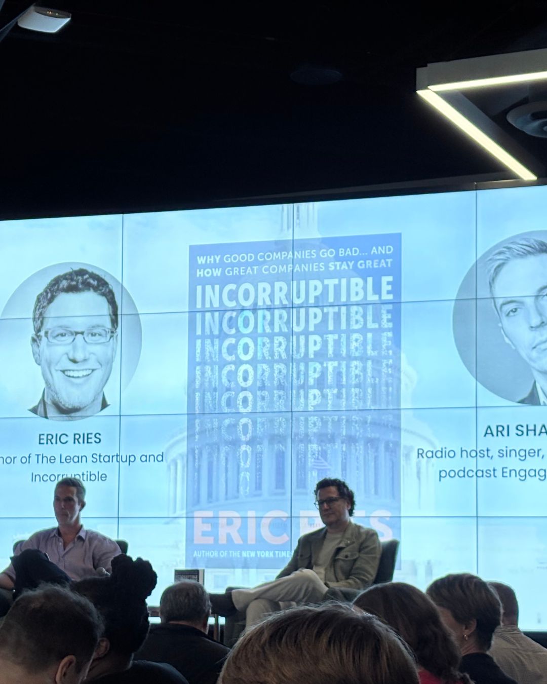 Candid shot from the audience: Eric and Ari mid-conversation, with attendees in the foreground