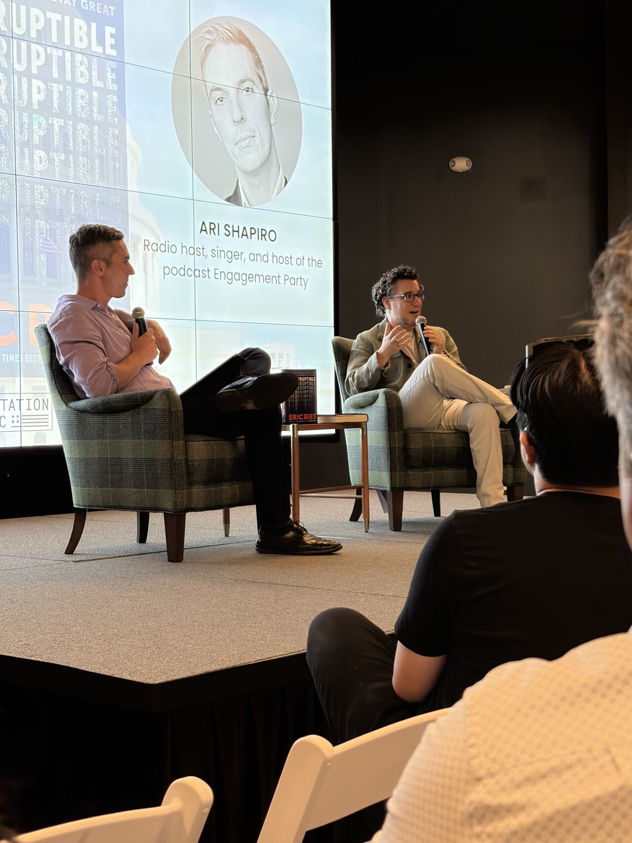 Wide shot of the STATION DC stage with Eric and Ari seated below the Incorruptible cover and host portraits