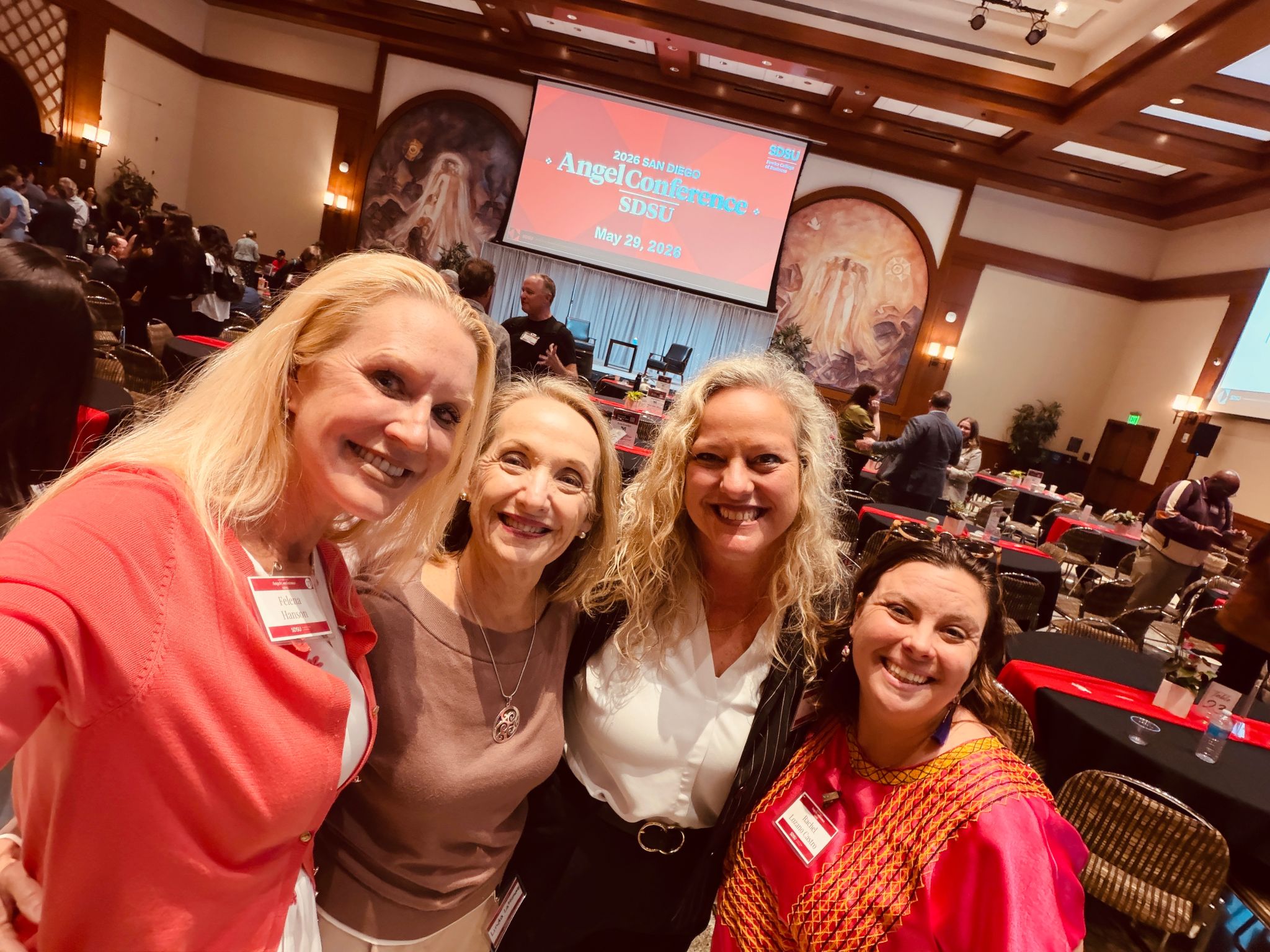 Group selfie of four SDAC attendees in front of the Angel Conference signage